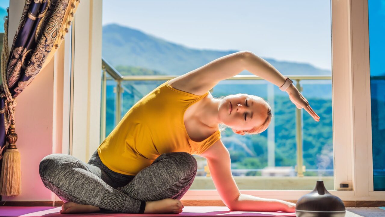 Mindful healthy woman practicing yoga at home. Sitting on the floor doing yoga for mental balance relaxing on stress. Enjoying time uses an aroma diffuser