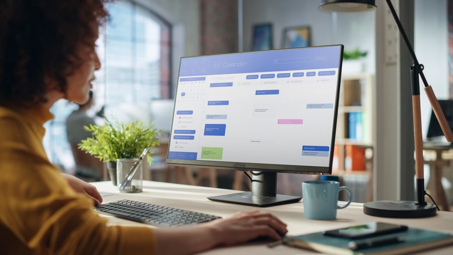 Portrait of a Happy Middle Eastern Manager Working in Creative Office. Business-Driven Stylish Female with Curly Hair Using Desktop Computer with a Calendar Software on Screen Display.
