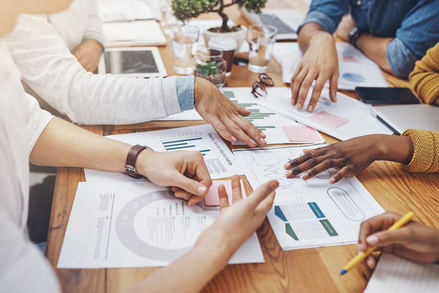 Team, hands and documents in office for meeting, budget planning and networking strategy. Business people, finance paper and tech at table for research analysis, projection or creative startup report